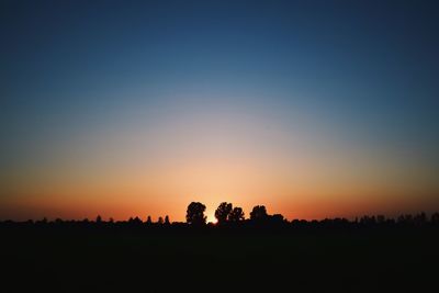 Silhouette trees on landscape against clear sky