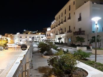 Illuminated street amidst buildings against sky at night