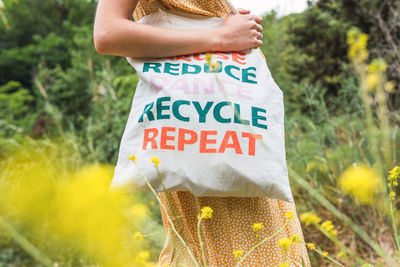 Side view of cropped unrecognizable female standing with eco friendly textile bag in summer park