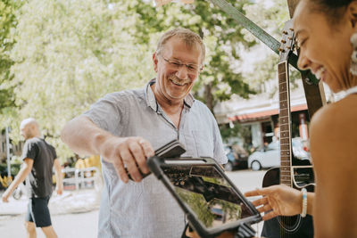 Happy senior male customer paying through contactless payment while shopping at flea market