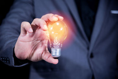 Midsection of businessman holding illuminated light bulb