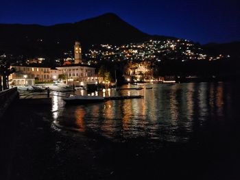 Illuminated buildings by sea against sky at night