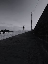 Man holding fishing rod walking on land against sky