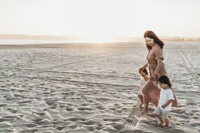 Side view of mother walking toddler twins to ocean with sun setting negative space