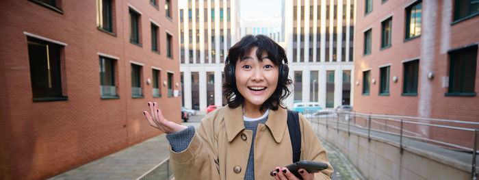 Portrait of young woman standing against building