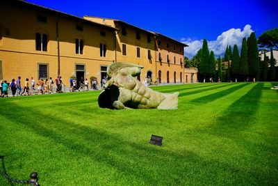 People relaxing on lawn by building against sky