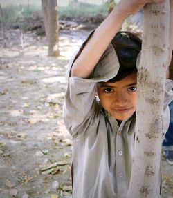 Portrait of smiling boy holding tree trunk while standing on field