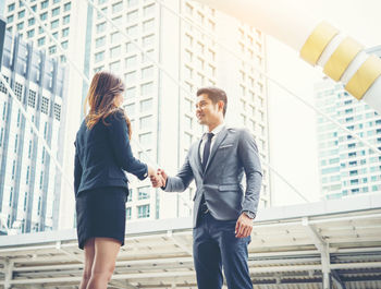 Smiling colleagues handshaking while standing against buildings in city