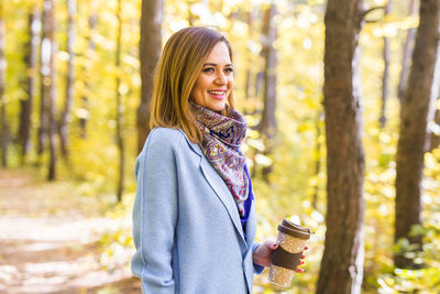 Portrait of smiling woman standing in forest during autumn