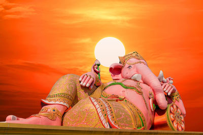 Low angle view of female statue against orange sky