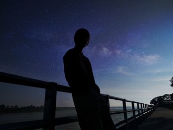 Silhouette man standing by railing against clear sky at night