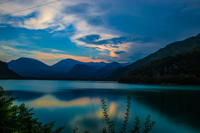 Scenic view of lake by mountains against cloudy sky during sunset