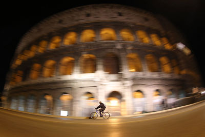 Low angle view of man riding bicycle against coliseum at night