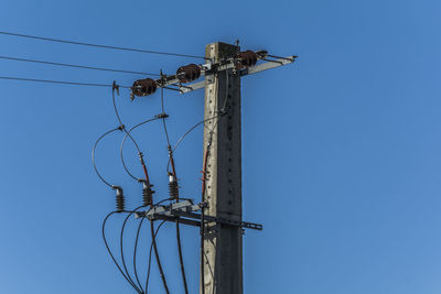 Low angle view of electricity pylon against clear blue sky