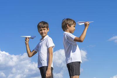 Low angle view of friends standing against blue sky