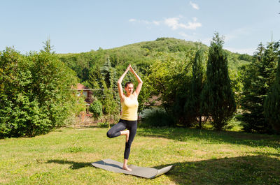 Full length of woman doing yoga on grassy field during sunny day