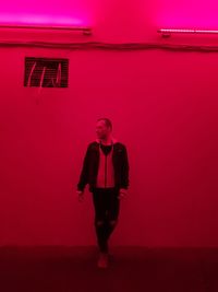 Portrait of young man standing against red wall