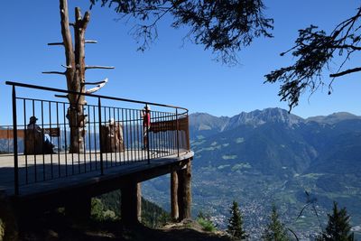 People at observation point by mountains against clear blue sky