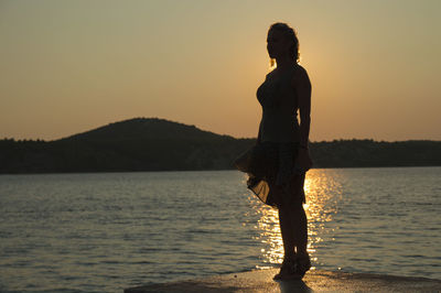 Woman standing at beach against sky during sunset