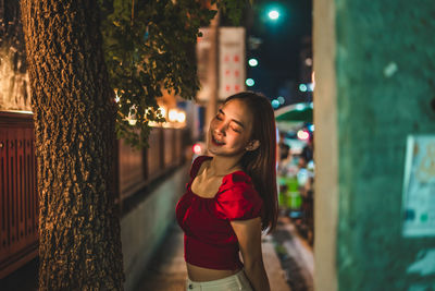 Young woman standing on sidewalk in city at night