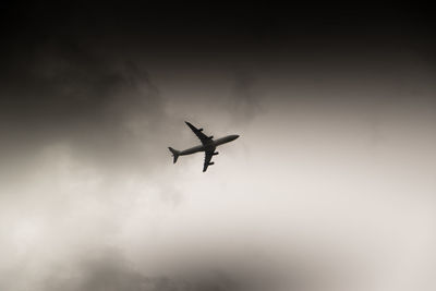 Low angle view of airplane flying in cloudy sky