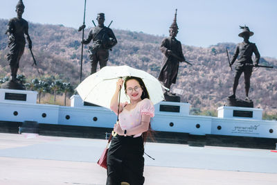 Smiling women holding umbrella standing against statue