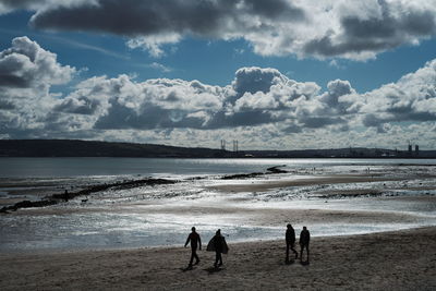 Silhouette people standing on beach against sky