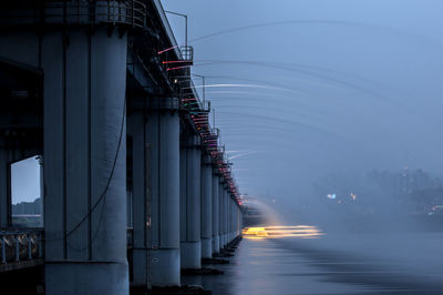 Low angle view of water flowing from bridge in river against sky at dusk