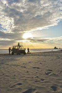 People on beach against sky during sunset