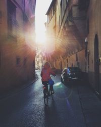 Rear view of man riding bicycle on street amidst buildings in city