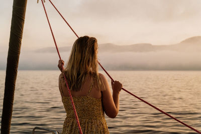 Rear view of woman standing by sea against sky