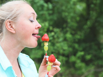 Beautiful blonde woman holding licking fruit barbecue skewers.