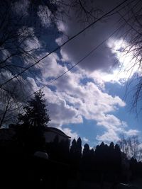 Low angle view of bare trees against cloudy sky