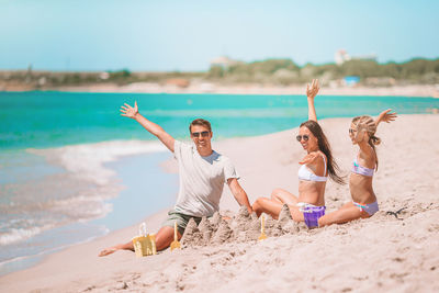 Cheerful family sitting on sand against sea