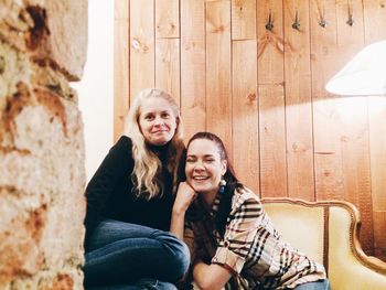 Portrait of happy female friends sitting against wooden wall
