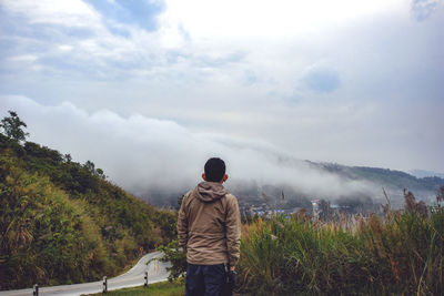 Rear view of man standing on mountain against sky