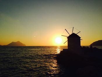 Wind turbine by sea against sky during sunset