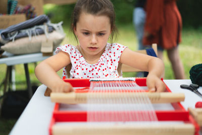 Girl weaving small rug with pattern at masterclass on weaving.