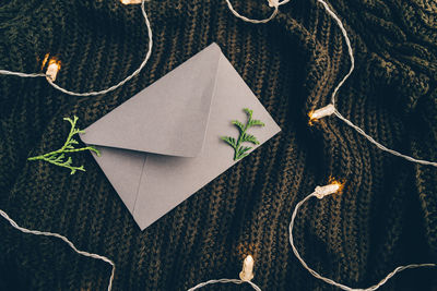 High angle view of string lights by envelope with leaves on woolen fabric