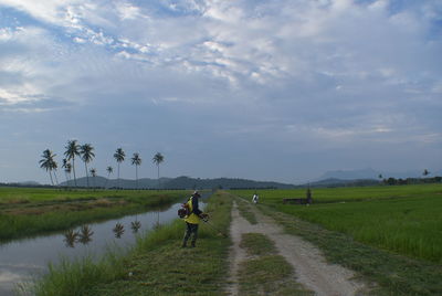 People on road amidst field against sky