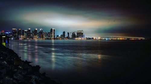 Illuminated buildings by sea against sky at night