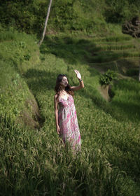 Young woman shielding eyes from sun while standing on field