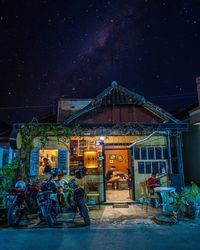 People in illuminated building against sky at night