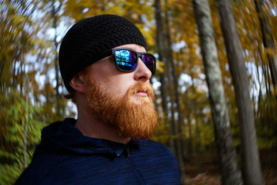 Bearded man wearing sunglasses and knit hat against trees