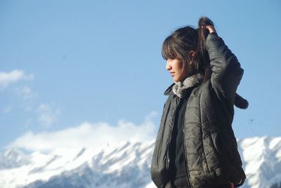 Side view of young woman standing against sky