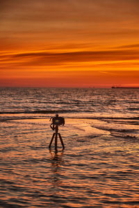 Rear view of silhouette woman standing on sea against sky during sunset