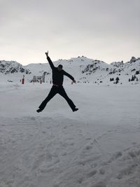 Man jumping on snowcapped mountain against sky