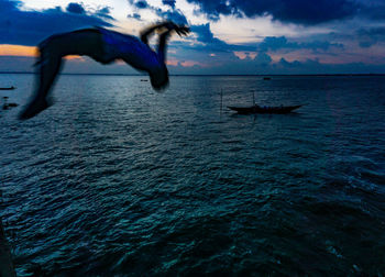 Man in sea against sky during sunset