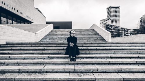 Thoughtful woman sitting on staircase against sky