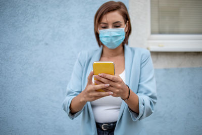 Midsection of woman holding mobile phone while standing at home